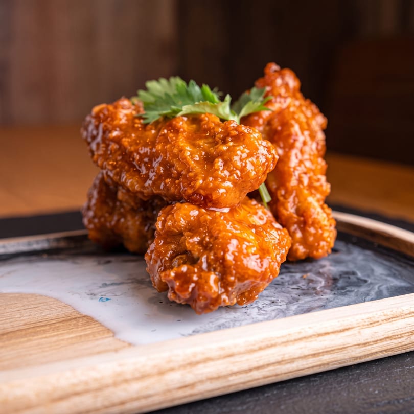 Glossy orange chicken wings with parsley garnish on a marbled plate with white sauce.