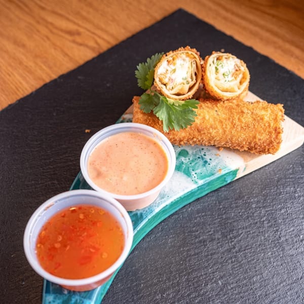 Crispy fried rolls, one halved, with two dipping sauces on a dark serving board.