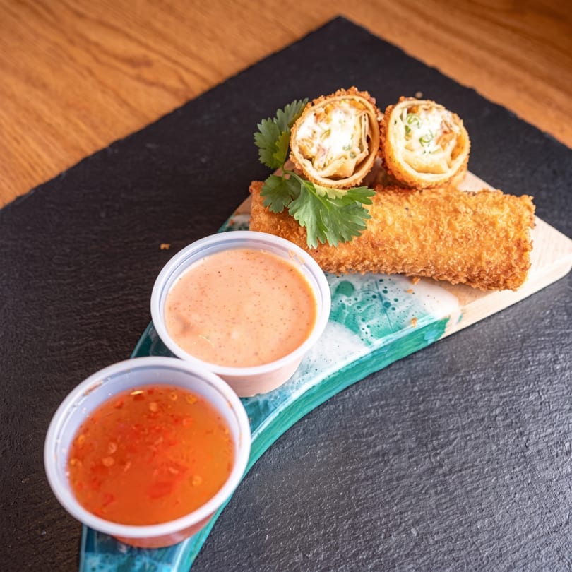 Crispy fried rolls, one halved, with two dipping sauces on a dark serving board.