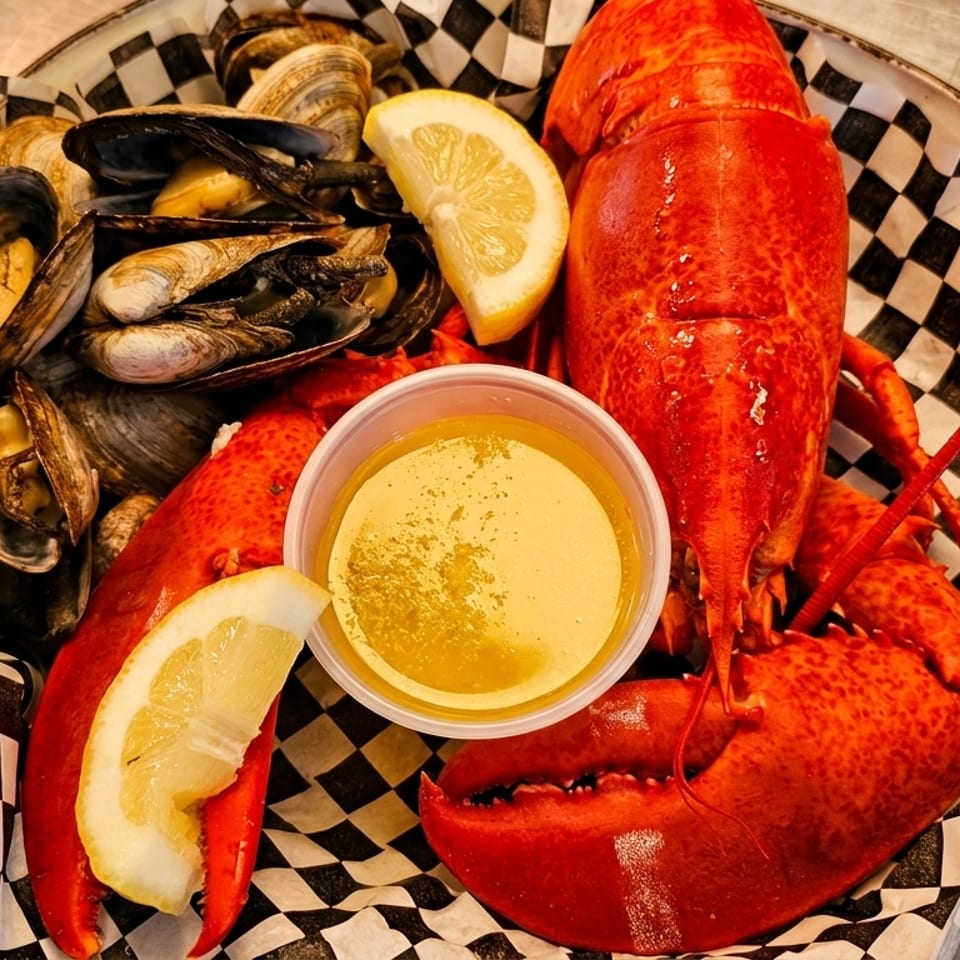 A seafood platter with a whole lobster, mussels, clams, lemon wedges, and butter sauce.