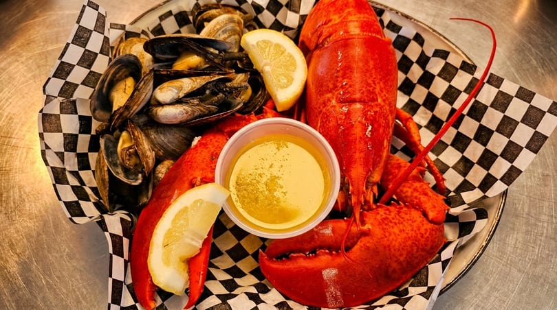 A seafood platter with a whole lobster, mussels, clams, lemon wedges, and butter sauce.