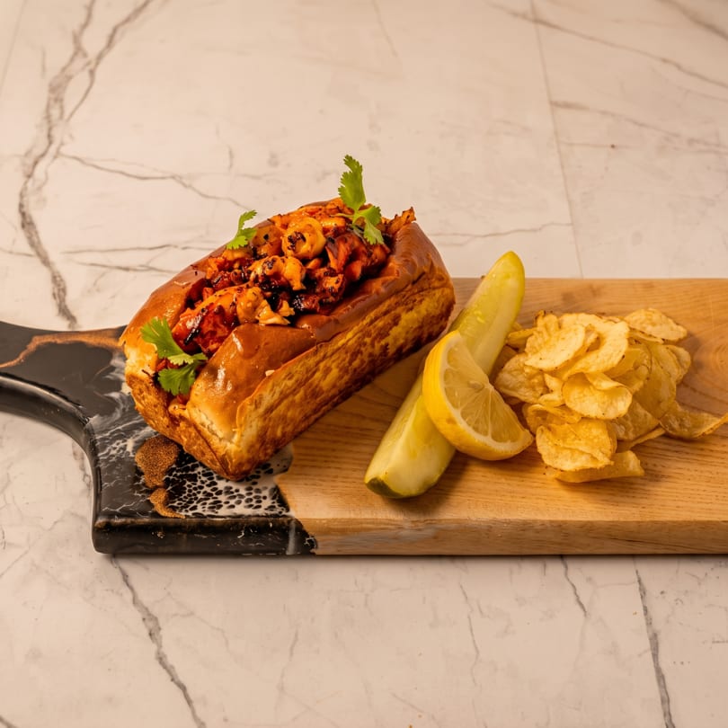 Grilled shrimp roll with cilantro, lemon, pickle, and potato chips on a marble and wood board.