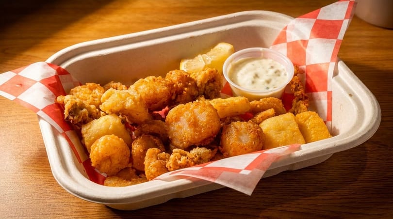 Fried seafood platter with scallops, clams, and hushpuppies, served with tartar sauce and lemon.