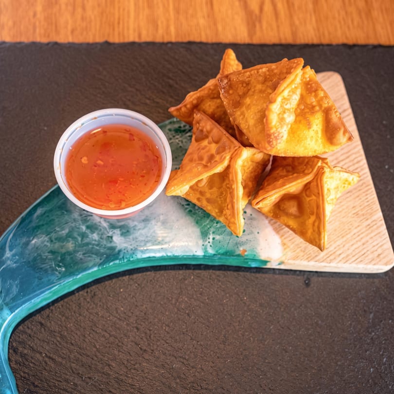 Golden fried wontons and a cup of sweet chili sauce on a decorative serving board.